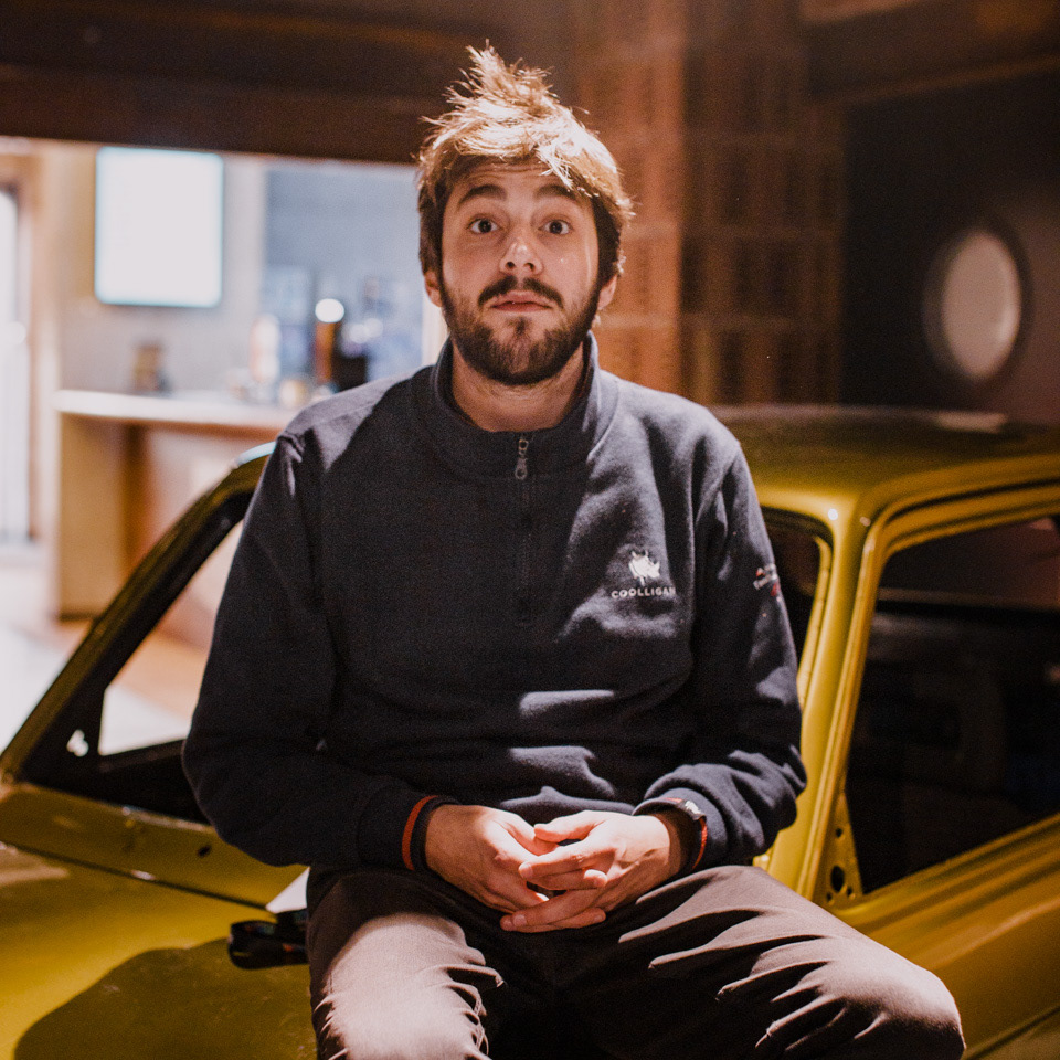 Salvador Sobral sits on the roof of a golden Maluch, looking straight into the camera lens in an artistic pose.